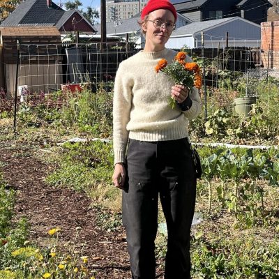 Cass standing in garden with flowers, red hat, sweater