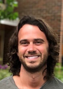 Christopher, in front of a brick building, smiling.