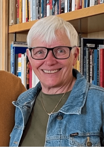 Judy standing in front of bookcase, smiling.